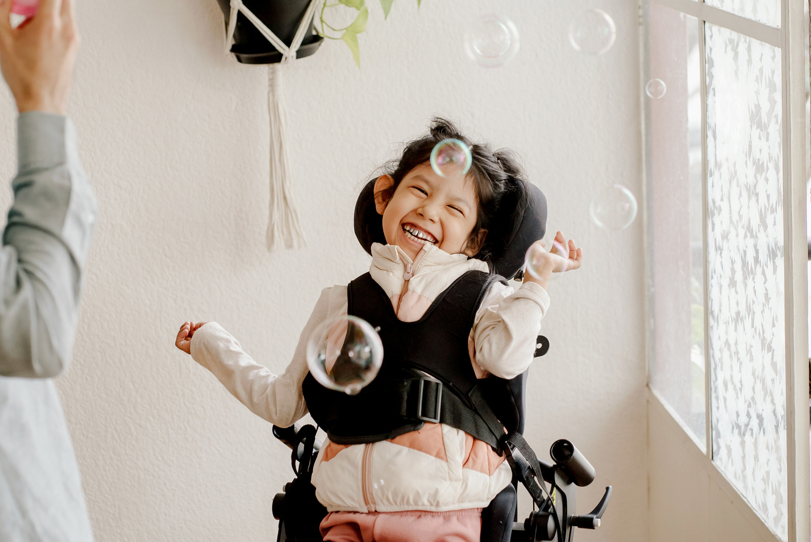 Child in Wheelchair Smiling While Playing With Bubbles Indoors